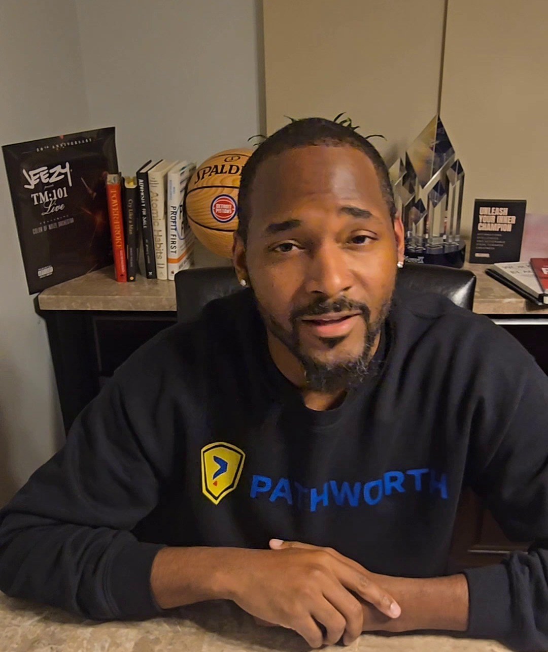 Jermaine Peguese at his desk in a Pathworth sweatshirt, looking into the camera