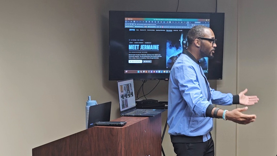 Jermaine Peguese in front of a wall screen, showing a room the website he built