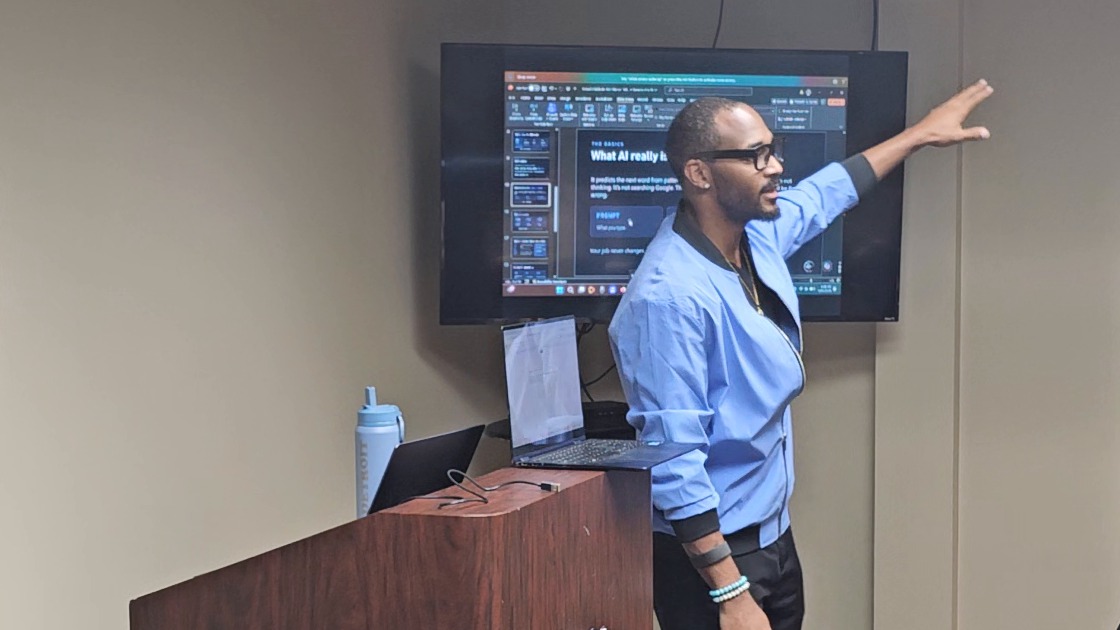 Jermaine Peguese teaching a workshop, pointing at a slide titled What AI really is